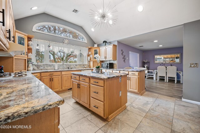 kitchen featuring kitchen peninsula, stainless steel appliances, a notable chandelier, a center island, and lofted ceiling