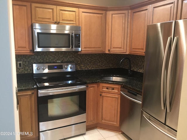 kitchen featuring sink, decorative backsplash, dark stone countertops, light tile patterned floors, and appliances with stainless steel finishes