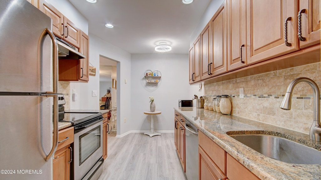 kitchen with backsplash, sink, light hardwood / wood-style flooring, light stone counters, and stainless steel appliances