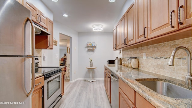 kitchen with backsplash, sink, light hardwood / wood-style flooring, light stone counters, and stainless steel appliances