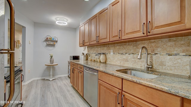 kitchen featuring sink, light stone countertops, light wood-type flooring, appliances with stainless steel finishes, and tasteful backsplash