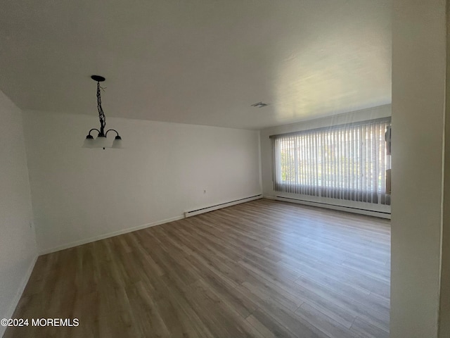 unfurnished living room with wood-type flooring, a baseboard radiator, and an inviting chandelier