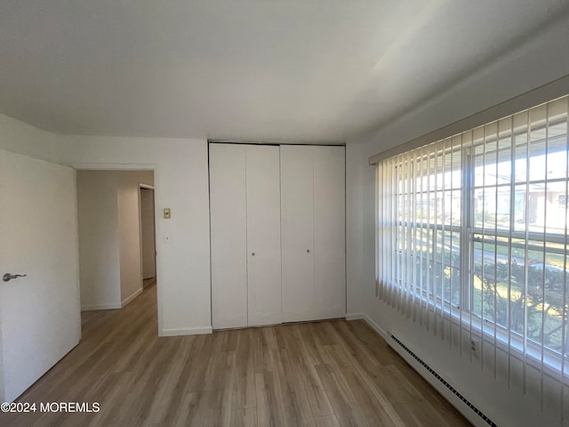 unfurnished bedroom with a closet, light hardwood / wood-style floors, and baseboard heating