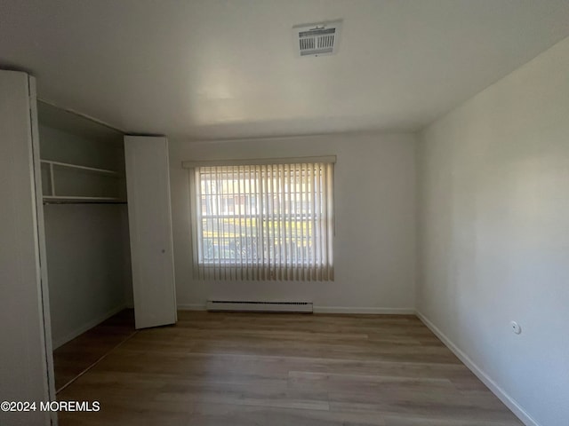 unfurnished bedroom featuring a closet, a baseboard radiator, and light wood-type flooring