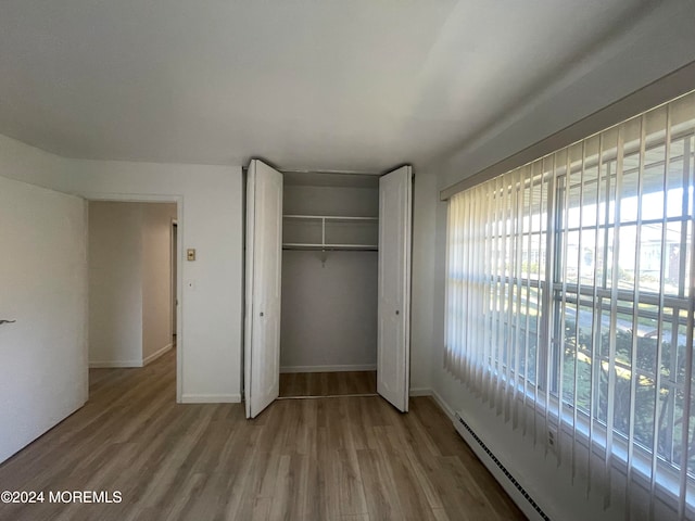 unfurnished bedroom featuring light hardwood / wood-style floors, baseboard heating, and a closet