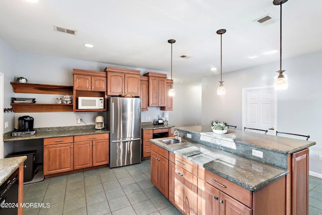 kitchen with stainless steel refrigerator, a center island with sink, hanging light fixtures, and sink