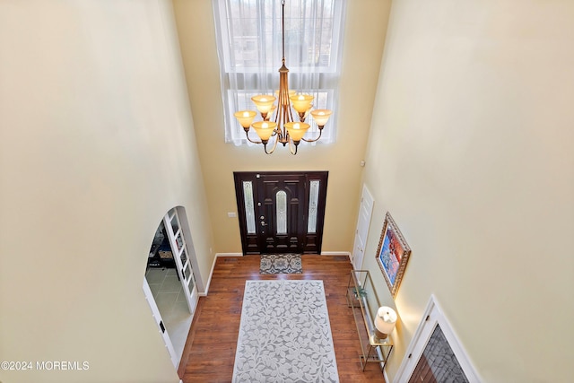 entryway featuring a towering ceiling, dark wood-type flooring, and an inviting chandelier