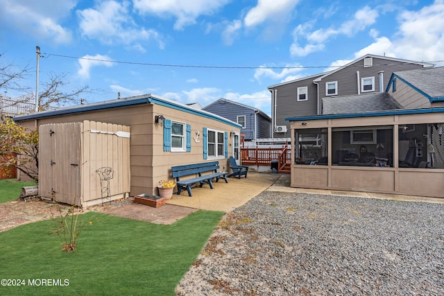 back of house featuring a sunroom, a yard, a storage unit, a wooden deck, and a patio area