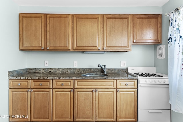 kitchen with dark stone countertops, sink, and white gas range oven