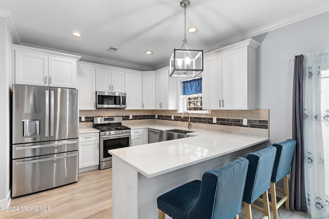 kitchen featuring appliances with stainless steel finishes, light wood-type flooring, sink, pendant lighting, and white cabinetry