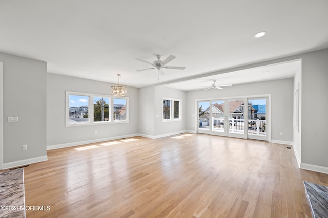 unfurnished living room with ceiling fan with notable chandelier, light hardwood / wood-style flooring, and a healthy amount of sunlight