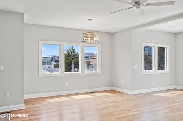 empty room with ceiling fan with notable chandelier and light hardwood / wood-style flooring