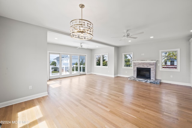 unfurnished living room with ceiling fan with notable chandelier, light hardwood / wood-style floors, and a fireplace