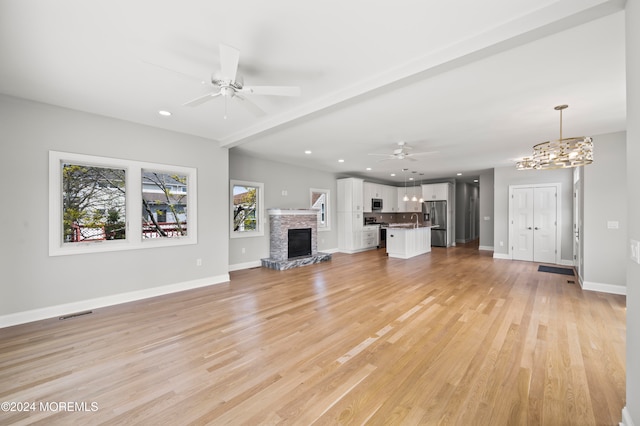 unfurnished living room with a fireplace, ceiling fan with notable chandelier, and light wood-type flooring