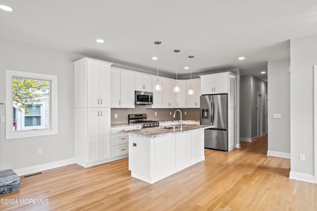 kitchen featuring pendant lighting, stainless steel appliances, a center island with sink, and light hardwood / wood-style floors