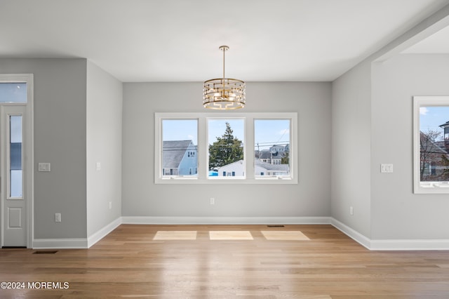 unfurnished dining area with a notable chandelier, a wealth of natural light, and light hardwood / wood-style flooring