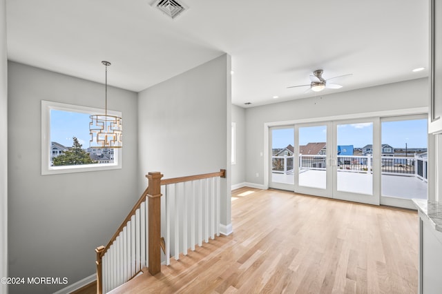 spare room with ceiling fan with notable chandelier and light wood-type flooring