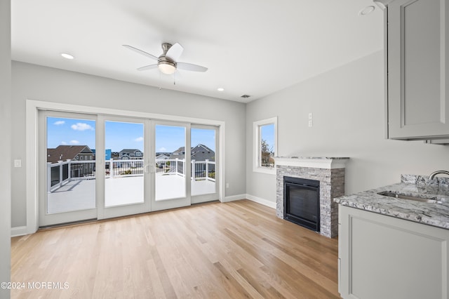 unfurnished living room featuring light hardwood / wood-style flooring, a stone fireplace, ceiling fan, and sink