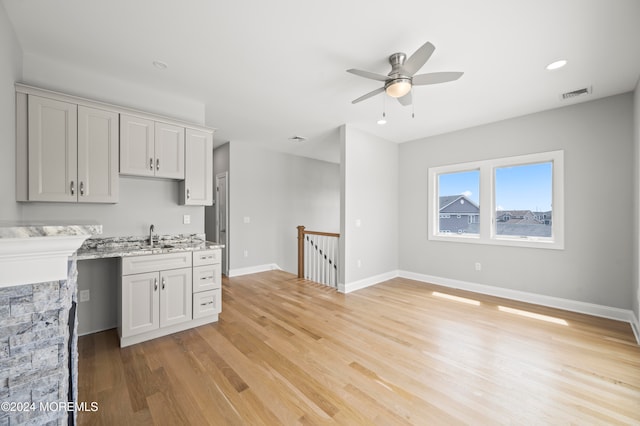 kitchen featuring light stone countertops, ceiling fan, sink, light hardwood / wood-style floors, and a fireplace