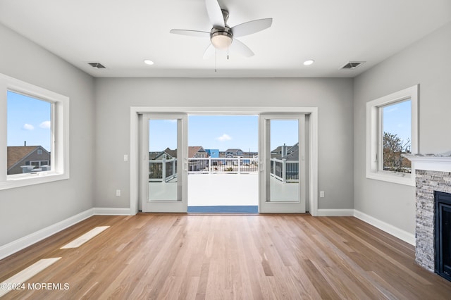 unfurnished living room with light hardwood / wood-style flooring, plenty of natural light, a stone fireplace, and ceiling fan