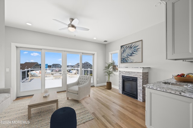 living room with a fireplace, light wood-type flooring, ceiling fan, and sink