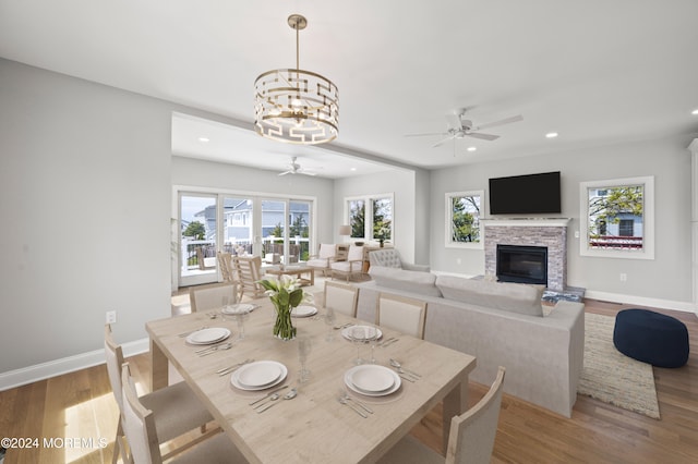 dining space with a fireplace, ceiling fan with notable chandelier, and light hardwood / wood-style floors