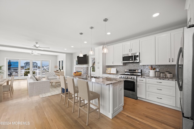 kitchen with decorative light fixtures, stainless steel appliances, white cabinetry, and an island with sink