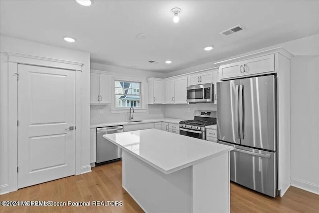 kitchen featuring white cabinets, a center island, stainless steel appliances, and light hardwood / wood-style flooring