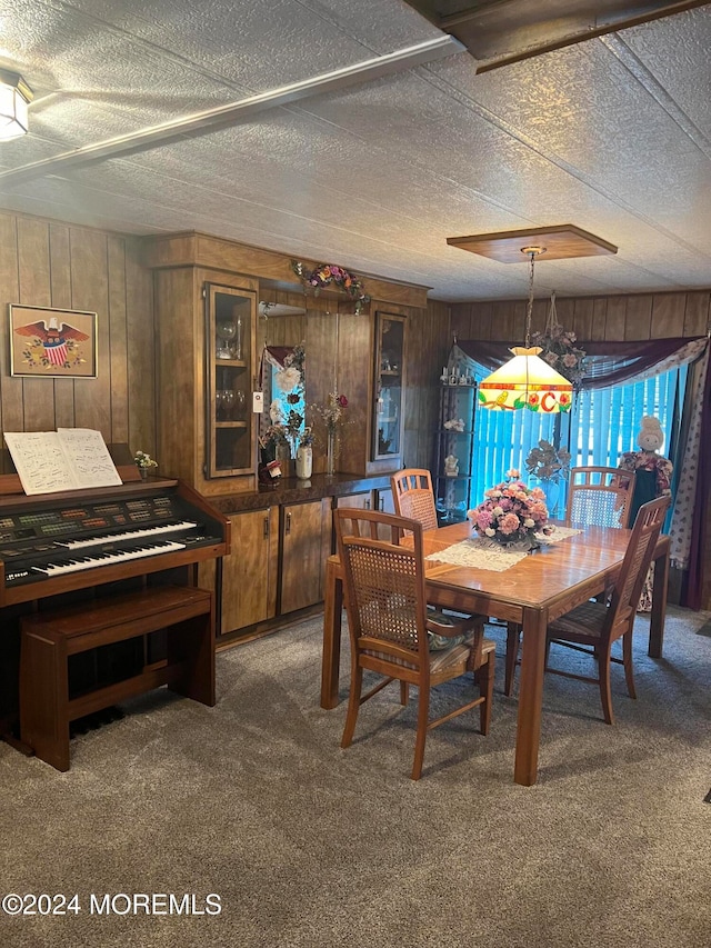 dining room featuring a textured ceiling, dark carpet, and wooden walls