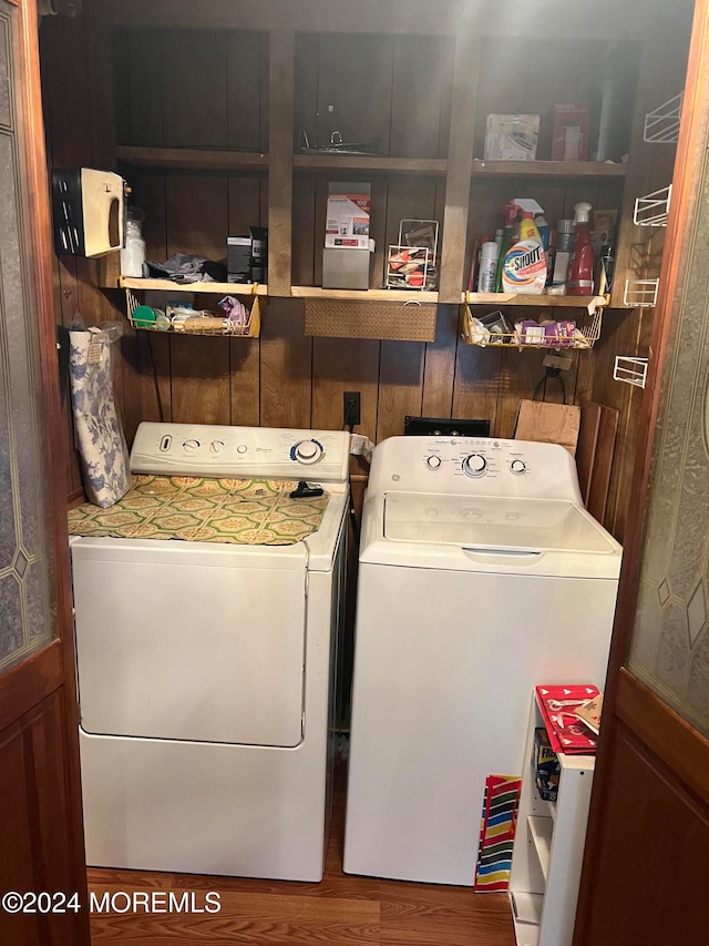 laundry area with washing machine and clothes dryer, wood walls, and hardwood / wood-style floors