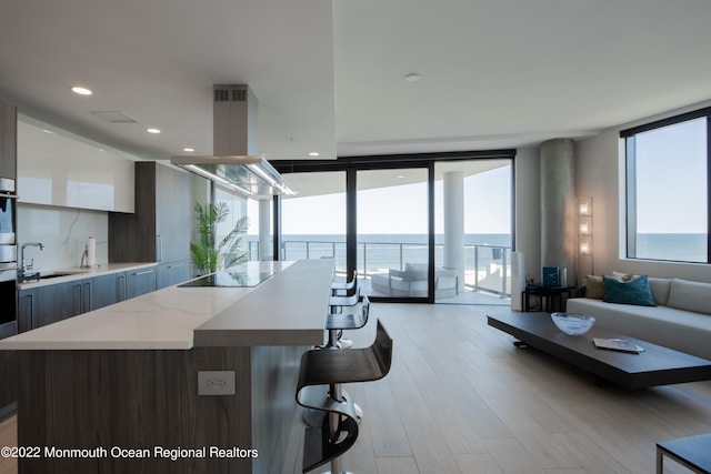 kitchen with sink, a water view, a wall of windows, a kitchen island, and island exhaust hood