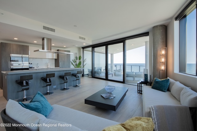 living room with floor to ceiling windows, a water view, and light hardwood / wood-style flooring