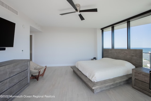 bedroom featuring floor to ceiling windows, a water view, ceiling fan, and light hardwood / wood-style flooring