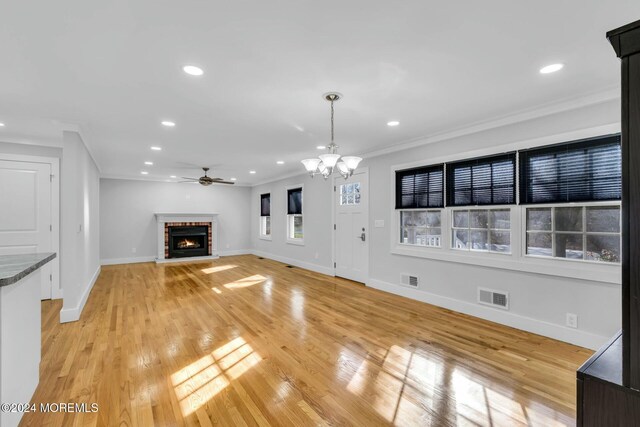 unfurnished living room with crown molding, light hardwood / wood-style floors, ceiling fan with notable chandelier, and a brick fireplace