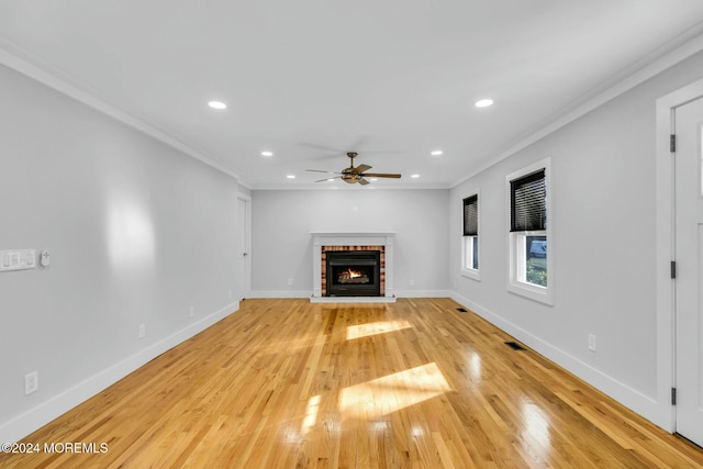 unfurnished living room with a brick fireplace, ceiling fan, ornamental molding, and light hardwood / wood-style flooring