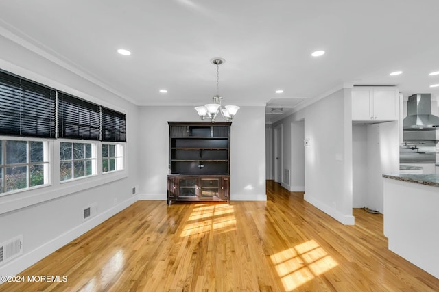 unfurnished dining area with crown molding, light hardwood / wood-style floors, and an inviting chandelier