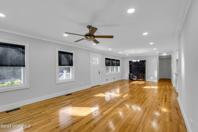 unfurnished living room with ceiling fan with notable chandelier, light hardwood / wood-style floors, plenty of natural light, and crown molding