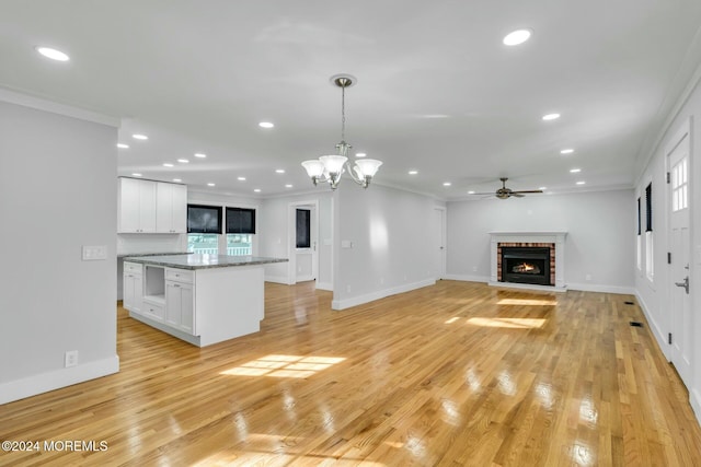 unfurnished living room featuring a brick fireplace, light hardwood / wood-style flooring, ceiling fan with notable chandelier, and ornamental molding