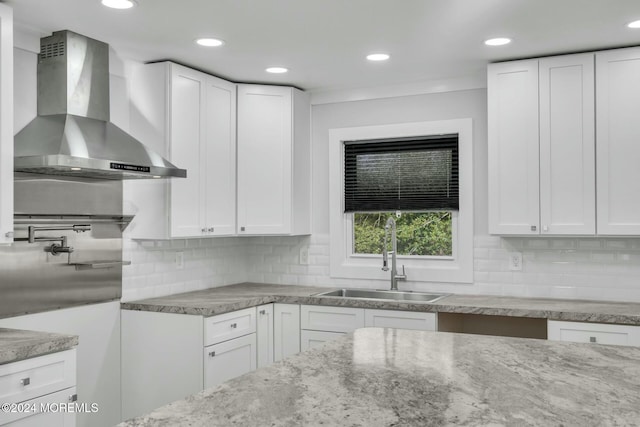 kitchen featuring white cabinets, wall chimney range hood, and backsplash