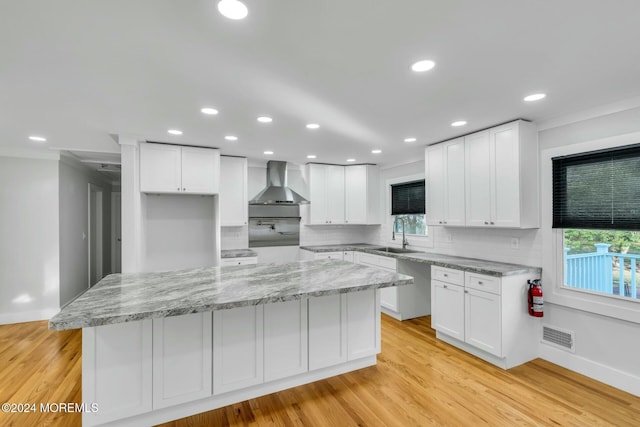 kitchen with white cabinets, wall chimney exhaust hood, a kitchen island, and light hardwood / wood-style floors