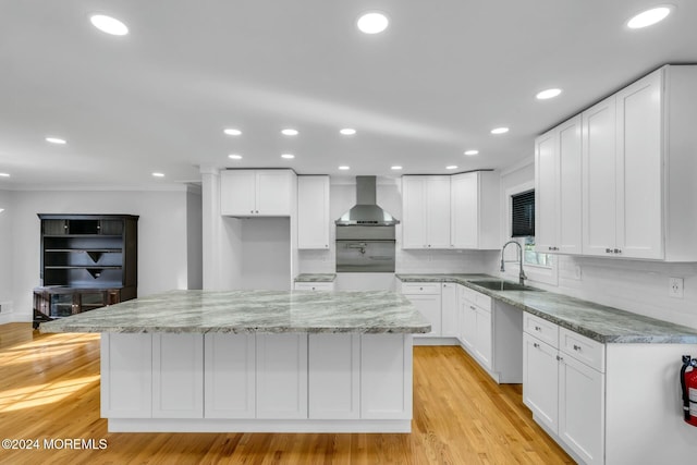 kitchen featuring white cabinets, a center island, wall chimney exhaust hood, and sink