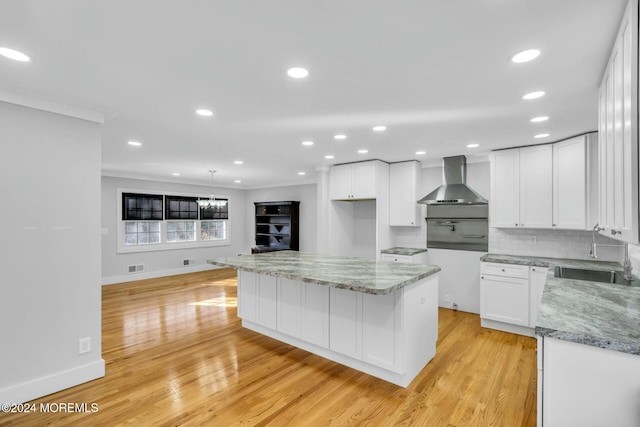 kitchen featuring white cabinetry, a center island, wall chimney exhaust hood, sink, and light hardwood / wood-style floors