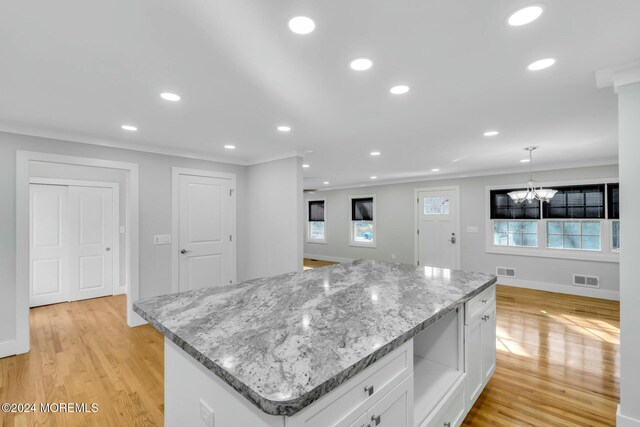 kitchen with white cabinetry, pendant lighting, light wood-type flooring, a kitchen island, and ornamental molding