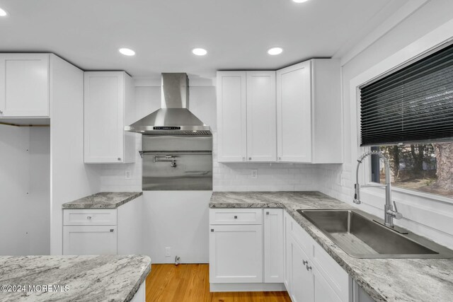 kitchen featuring white cabinets, light hardwood / wood-style flooring, wall chimney exhaust hood, and sink