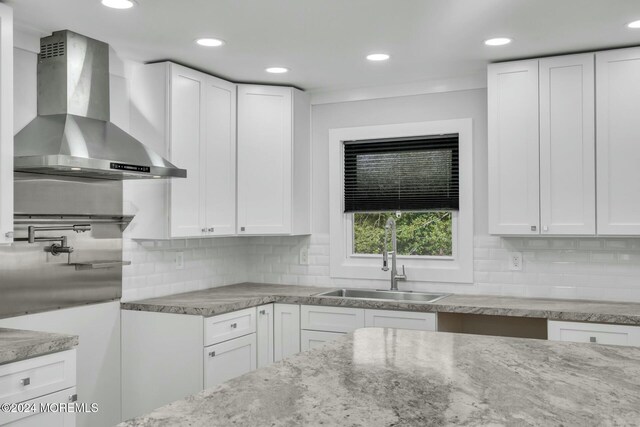 kitchen with decorative backsplash, white cabinetry, and wall chimney range hood