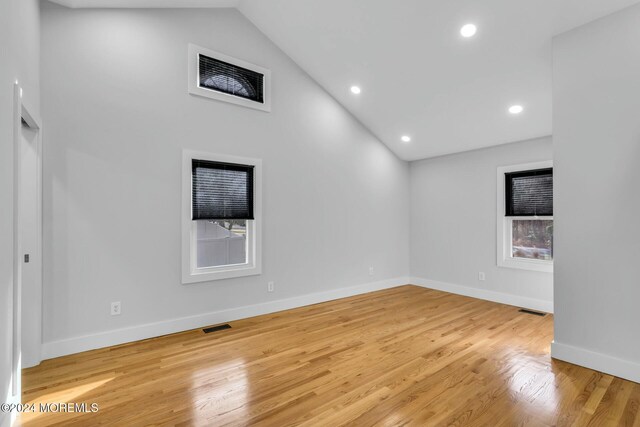 empty room with a healthy amount of sunlight, high vaulted ceiling, and light hardwood / wood-style floors