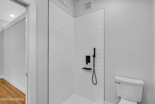 bathroom with hardwood / wood-style floors, toilet, and tiled shower