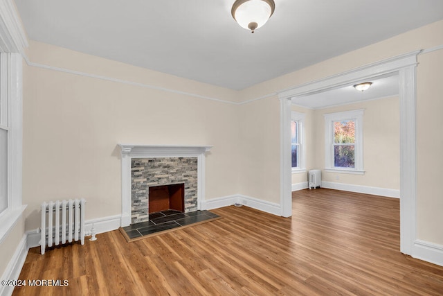 unfurnished living room featuring a tiled fireplace, radiator heating unit, and hardwood / wood-style floors