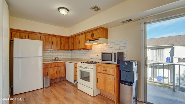 kitchen with tasteful backsplash, sink, light hardwood / wood-style floors, and white appliances