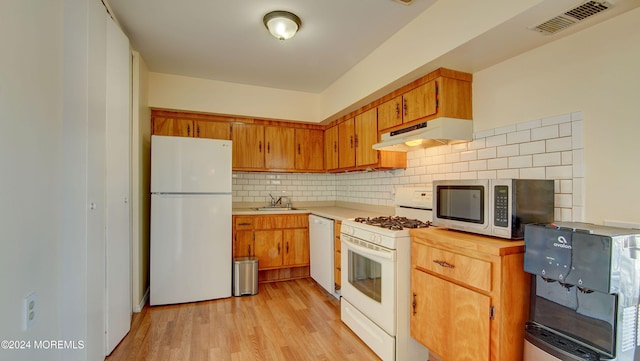 kitchen featuring light wood-type flooring, white appliances, backsplash, and sink